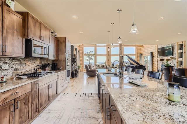 kitchen with light stone counters, stainless steel appliances, tasteful backsplash, open floor plan, and a sink