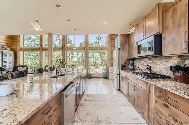 kitchen with light stone countertops, pendant lighting, stainless steel appliances, sink, and wooden walls