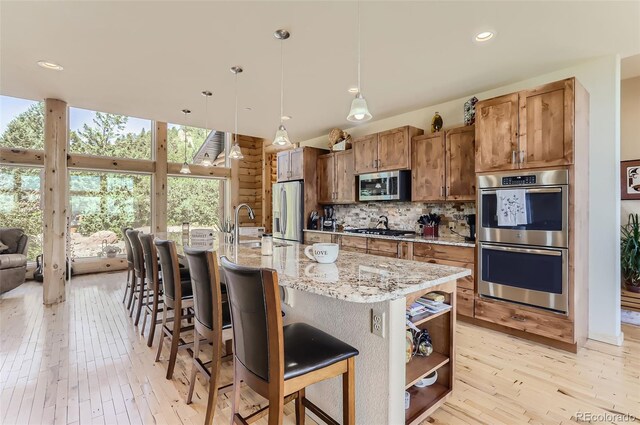 kitchen with an island with sink, light hardwood / wood-style flooring, stainless steel appliances, and light stone counters