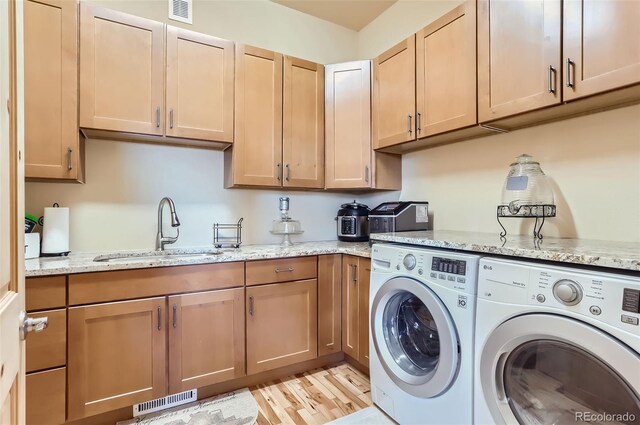 clothes washing area with light wood-type flooring, cabinets, sink, and washer and clothes dryer