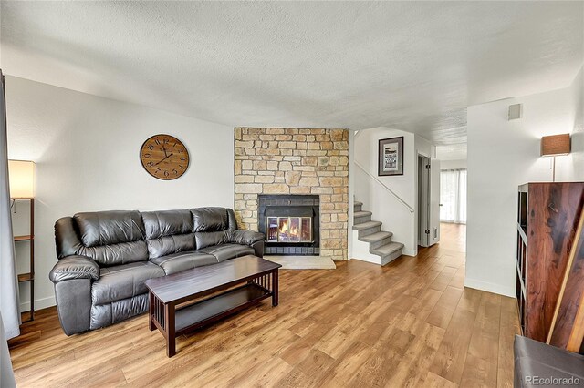 6765 S Independence St, Littleton, CO 80128 - living area with a stone fireplace, light wood-type flooring, a textured ceiling, stairs, and baseboards