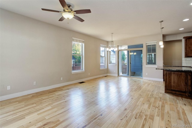 unfurnished dining area with ceiling fan with notable chandelier and light hardwood / wood-style flooring