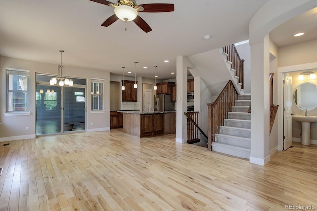 unfurnished living room with sink, ceiling fan with notable chandelier, and light hardwood / wood-style floors