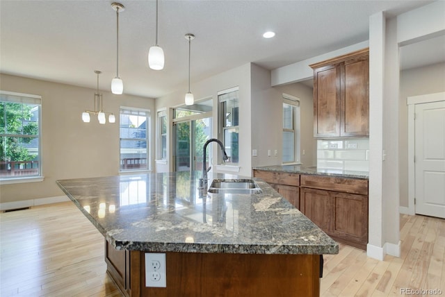 kitchen featuring a center island with sink, decorative light fixtures, sink, and light hardwood / wood-style floors