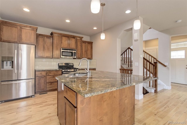 kitchen with appliances with stainless steel finishes, hanging light fixtures, sink, and light hardwood / wood-style flooring