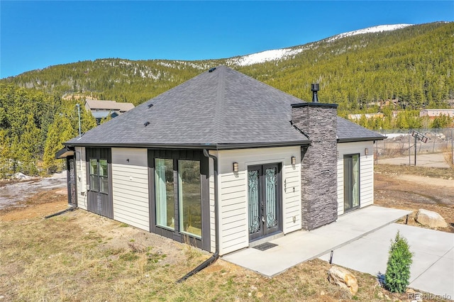 499 Silver Creek Rd, Idaho Springs, CO 80452 - back of house featuring a wooded view, a mountain view, roof with shingles, and a chimney