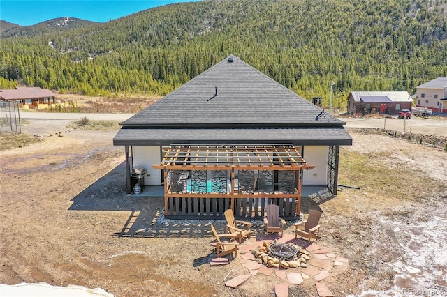 499 Silver Creek Rd, Idaho Springs, CO 80452 - rear view of property with a wooded view, roof with shingles, a mountain view, and an outdoor fire pit