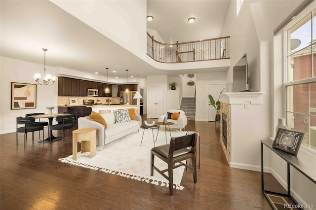 living room featuring stairs, dark wood-type flooring, a notable chandelier, and baseboards