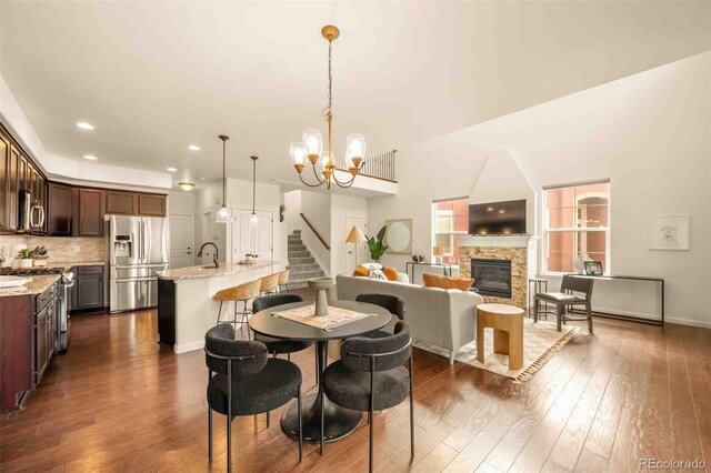 dining area featuring dark wood-style floors, an inviting chandelier, a fireplace, baseboards, and stairs