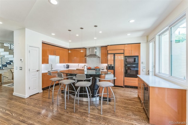 461 Fillmore St, Denver, CO 80206 - kitchen featuring black appliances, wall chimney exhaust hood, brown cabinetry, wood finished floors, and a kitchen island