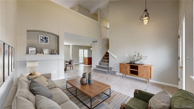 living room with baseboards, light tile patterned floors, visible vents, stairs, and a high ceiling