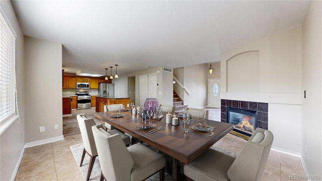 dining room featuring a tile fireplace, baseboards, light tile patterned floors, visible vents, and stairway