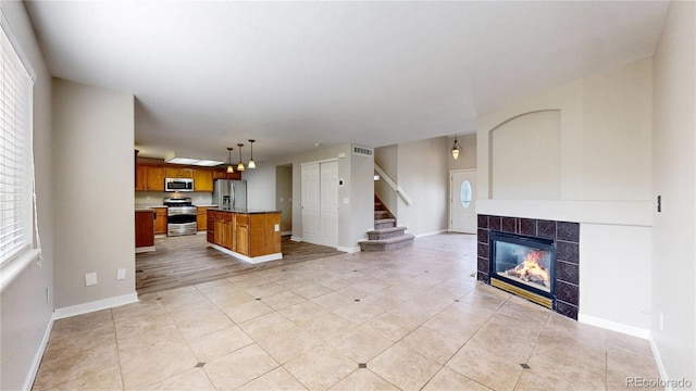 unfurnished living room featuring stairs, visible vents, light tile patterned floors, baseboards, and a tiled fireplace