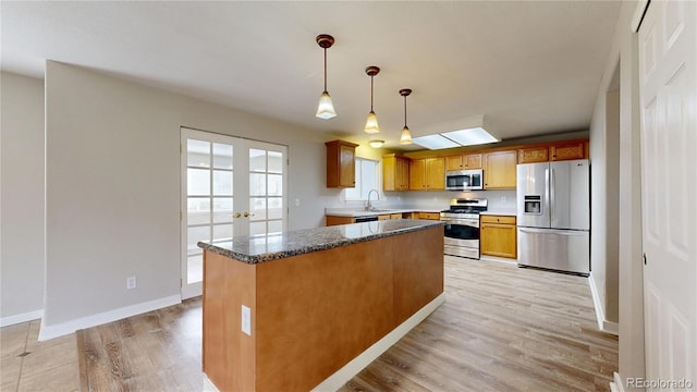 kitchen featuring a sink, light wood-style flooring, hanging light fixtures, baseboards, and appliances with stainless steel finishes