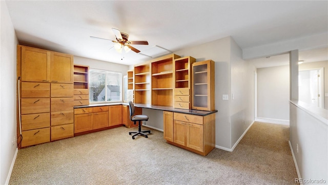 unfurnished office featuring built in study area, light carpet, baseboards, and a ceiling fan