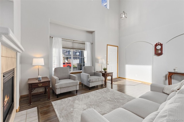 living room featuring a glass covered fireplace, plenty of natural light, light wood-type flooring, a high ceiling, and baseboards