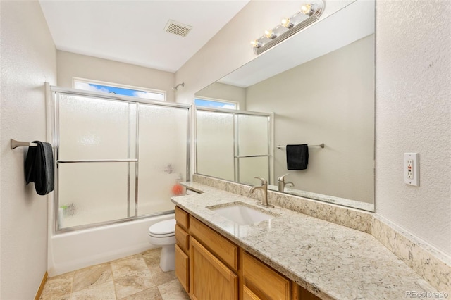 full bath with vanity, toilet, shower / bath combination with glass door, and stone finish floors