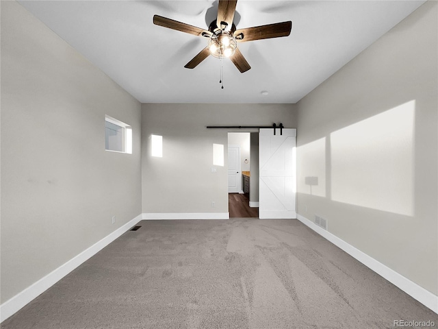 carpeted spare room with a barn door and ceiling fan