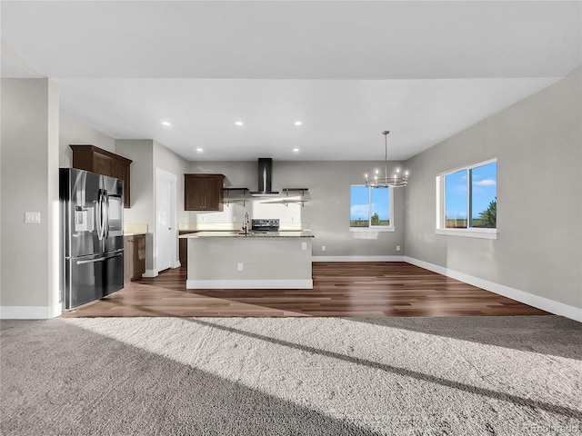 kitchen featuring wall chimney exhaust hood, dark colored carpet, black fridge, a chandelier, and pendant lighting