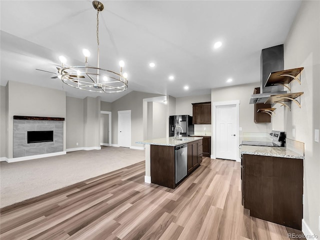 kitchen with an inviting chandelier, black fridge, light hardwood / wood-style flooring, stainless steel dishwasher, and a fireplace