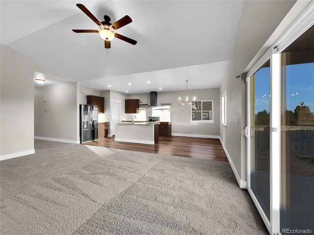 unfurnished living room with ceiling fan with notable chandelier, dark carpet, vaulted ceiling, and sink