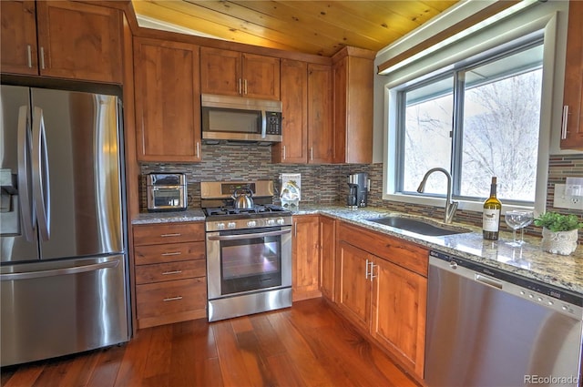 kitchen featuring a sink, appliances with stainless steel finishes, decorative backsplash, light stone countertops, and dark wood-style flooring