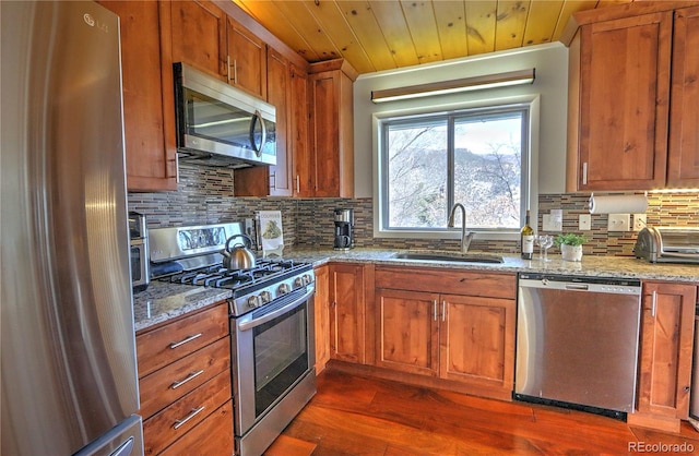 kitchen with brown cabinets, appliances with stainless steel finishes, light stone countertops, and a sink