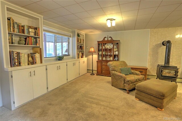 sitting room featuring a baseboard heating unit, a wood stove, baseboard heating, and light carpet