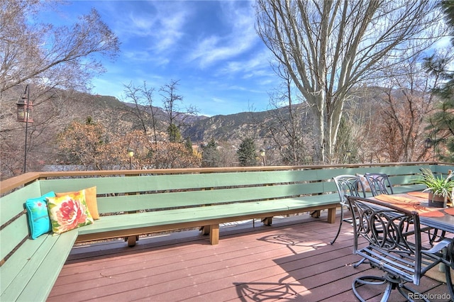 wooden terrace with outdoor dining space, a view of trees, and a mountain view