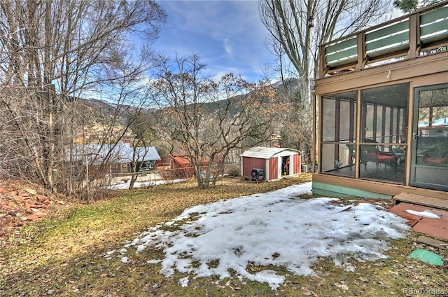 yard covered in snow featuring a storage shed, an outbuilding, fence, and a sunroom