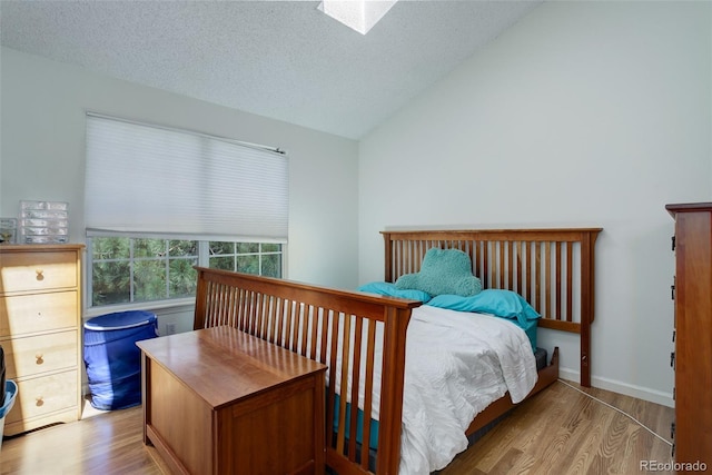 bedroom featuring a textured ceiling, vaulted ceiling with skylight, and light wood-type flooring