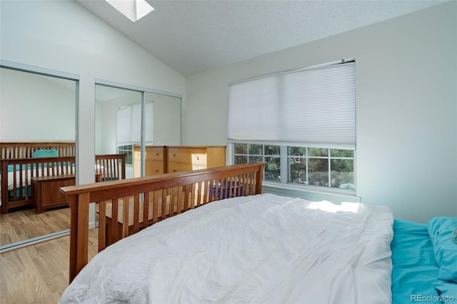 bedroom featuring vaulted ceiling with skylight, a textured ceiling, light hardwood / wood-style flooring, and two closets