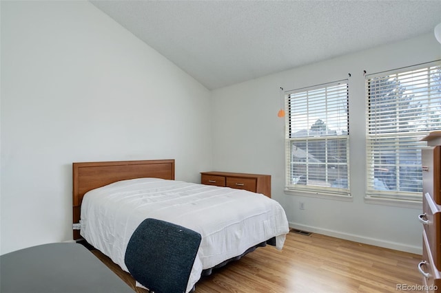 bedroom featuring vaulted ceiling, a textured ceiling, and light wood-type flooring