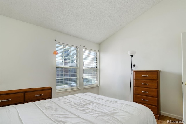 bedroom featuring lofted ceiling, hardwood / wood-style floors, and a textured ceiling