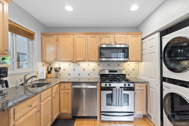 2967 Olive St, Denver, CO 80207 - kitchen with stainless steel appliances, stacked washer / dryer, a sink, dark stone countertops, and light brown cabinets
