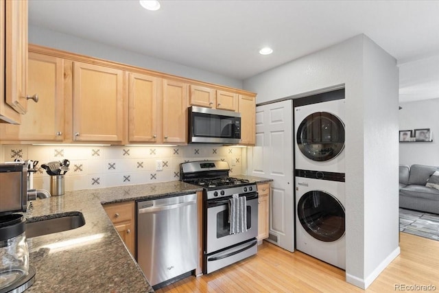 2967 Olive St, Denver, CO 80207 - kitchen with stainless steel appliances, stacked washer / drying machine, decorative backsplash, dark stone counters, and light wood finished floors