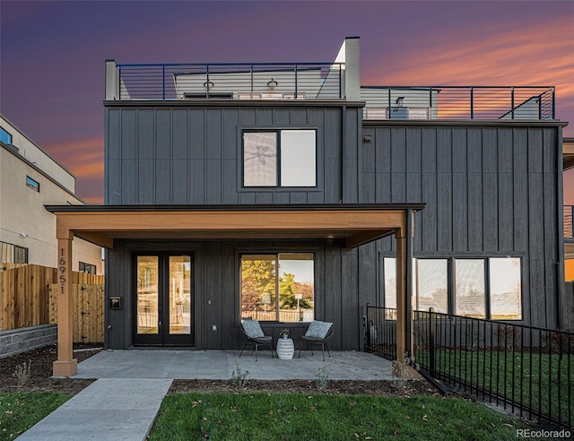 back house at dusk with a patio area, french doors, a lawn, and a balcony