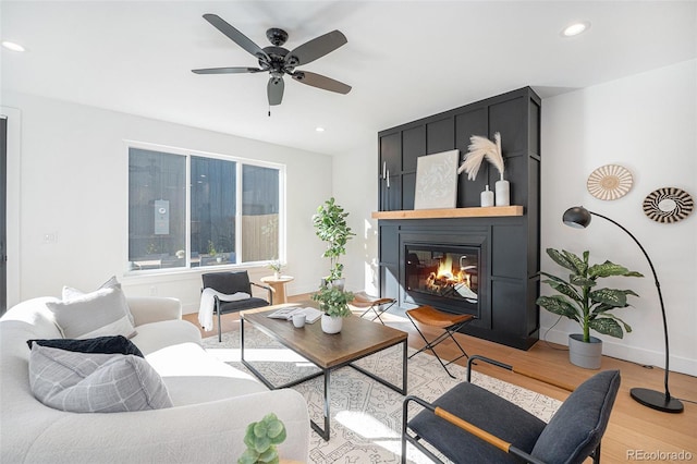 living room featuring a large fireplace, light hardwood / wood-style flooring, and ceiling fan