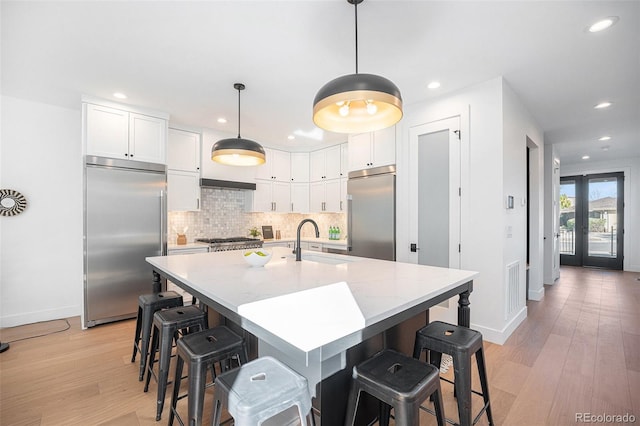 kitchen featuring sink, pendant lighting, white cabinetry, appliances with stainless steel finishes, and light hardwood / wood-style floors