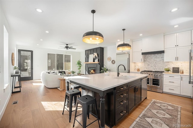 kitchen with sink, high end appliances, hanging light fixtures, custom range hood, and white cabinets