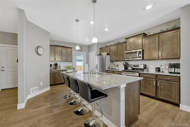 kitchen with appliances with stainless steel finishes, decorative light fixtures, a kitchen bar, light stone countertops, and a center island with sink