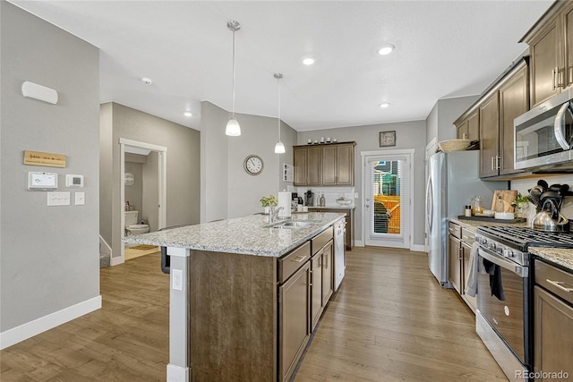 kitchen featuring sink, light stone counters, decorative light fixtures, a center island with sink, and stainless steel appliances