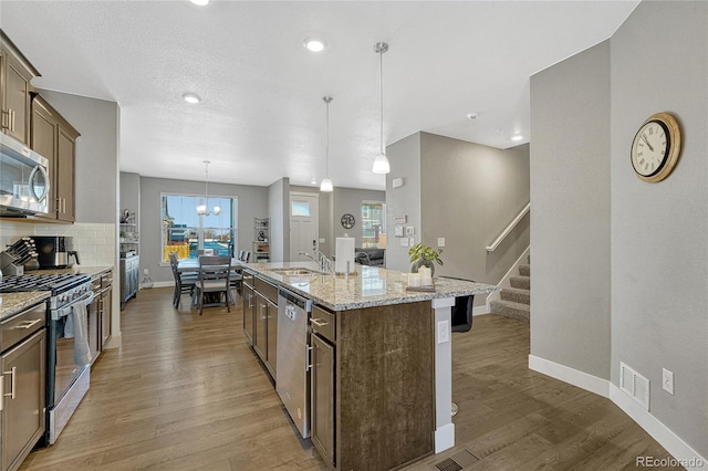 kitchen featuring tasteful backsplash, hanging light fixtures, a center island with sink, stainless steel appliances, and light stone countertops