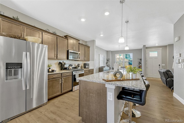 kitchen featuring a breakfast bar area, hanging light fixtures, a center island with sink, light wood-type flooring, and appliances with stainless steel finishes