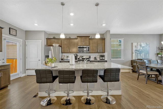 kitchen with appliances with stainless steel finishes, a kitchen breakfast bar, hanging light fixtures, and a center island with sink