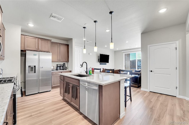 kitchen with sink, light hardwood / wood-style floors, a textured ceiling, a center island with sink, and appliances with stainless steel finishes