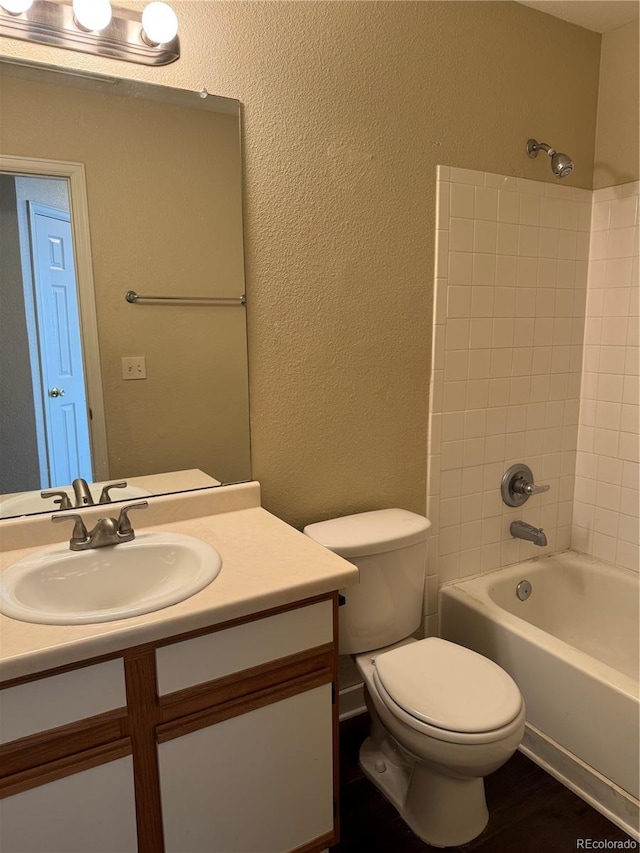 full bathroom with hardwood / wood-style flooring, vanity, tiled shower / bath, and toilet