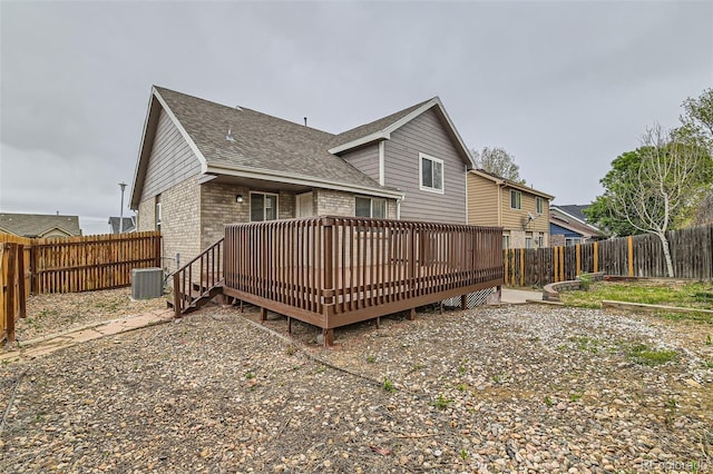 back of house featuring brick siding, central AC, a deck, roof with shingles, and a fenced backyard