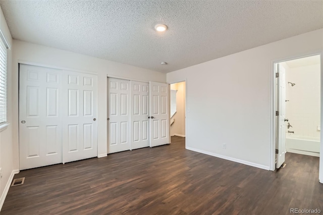 unfurnished bedroom with a textured ceiling, two closets, baseboards, and dark wood-style floors