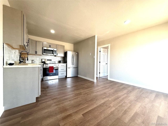 kitchen featuring appliances with stainless steel finishes, tasteful backsplash, light countertops, gray cabinetry, and dark wood-style floors